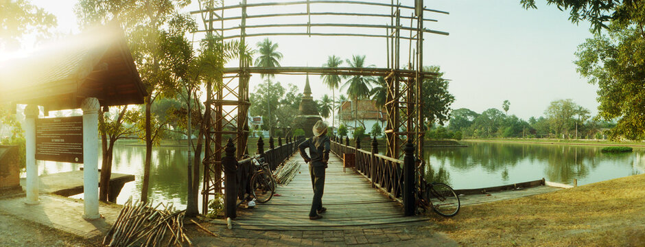 Panoramic view of man rebuilding the entrance to a wooden bridge leading to a Buddhist temple, Sukhothai Historical Park, Sukhothai, Thailand.