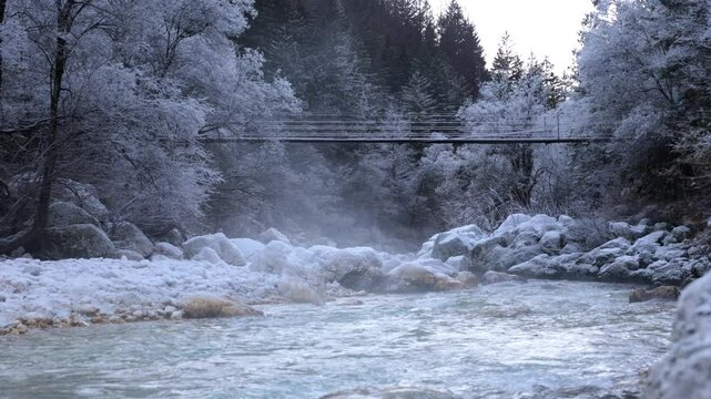 inquadratura fissa che mostra l'acqua gelida che scorre lungo le rive ghiacciate del fiume Isonzo, circondato da boschi, con del vapore che sale dal basso, in Slovenia, in inverno