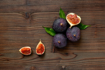 Fresh ripe figs whole and cut with green leaves on wooden table. Top view