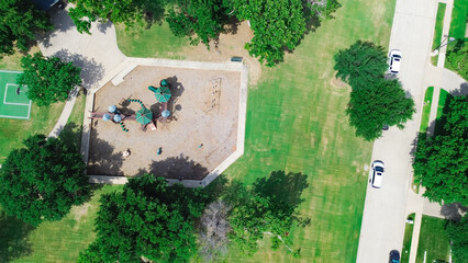 Suburban residential street near grassy community park with modern playground equipment structure,...