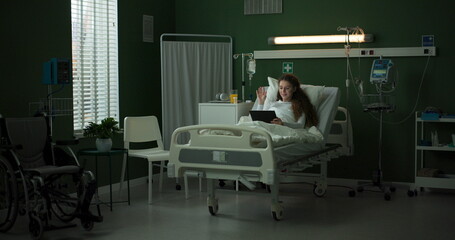 Patient in a hospital room uses a tablet while lying in bed.