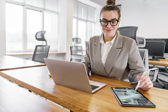 Professional woman working on laptop and tablet in modern office environment during day