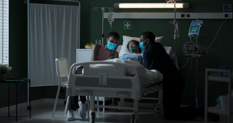 Young parents in masks sit next to their seriously ill daughter in intensive care.