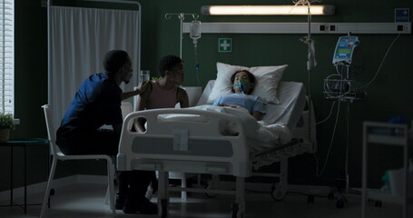 Young mother sits next to her child who is lying unconscious in an oxygen mask.