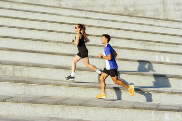 Couple of runners exercise energetically up outdoor stairs during early morning sunlight