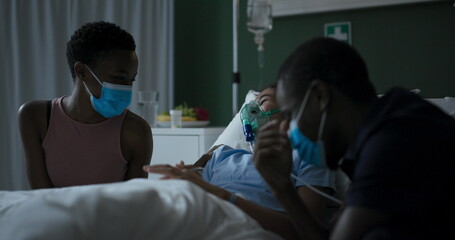 Family in hospital ward near ill child in bed.