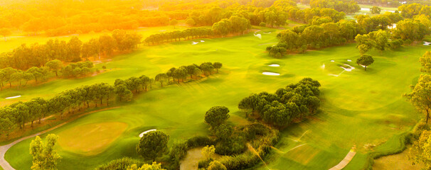 A panoramic view of a golf course bathed in golden sunset light surrounded by lush greenery
