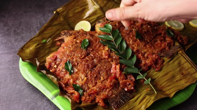 Kerala fish curry, Karimeen Pollichathu a popular hot and spicy baked fish in banana leaves Alleppey India. pearl spot fish is marinated with Indian spices then wrapped in plantain leaf and grilled.