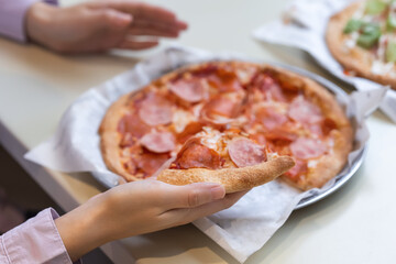 Woman eating delicious pepperoni pizza in casual diner. Reaches for a slice. Concept: Eating traditional Italian pizza in a restaurant. No face