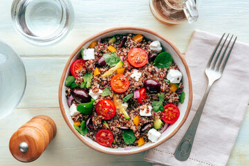 Quinoa salad, healthy Mediterranean lunch with fresh organic vegetables, cheese, and olives, shot from above on a wooden background