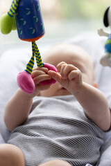 Newborn baby lying in a baby chair and playing curiously with hanging toys. Closeup, selective focus.
