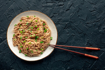 Soba, Japanese buckwheat noodles, boiled, on a plate on a black slate background, with chopsticks, a flat lay