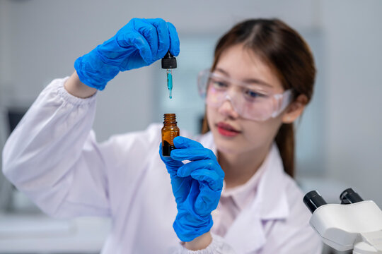 A woman in a lab coat is holding a bottle of blue liquid and a dropper