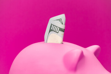 Close-up photo pink pig moneybox with dollars in it. Savings for retirement and personal finance concepts. One hundred dollar bill in pink piggy bank.