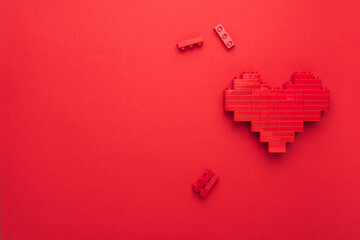 Top-down composition of toy emoji heart model with copy space. Minimalist photo of stylized red love symbol. Red heart symbol made of plastic building blocks with some of them left unused.