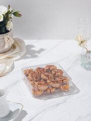 An elegant display of assorted pastries and drinks sits in a clear container on a marble surface, enhanced by floral arrangements