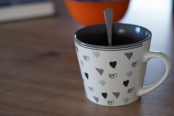 A drunk mug with hearts. There is a spoon in it and it is placed on the table.