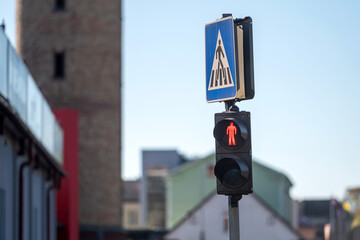 Traffic light displays red pedestrian signal next to city buildings during daylight hours
