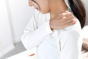 ベッドの上で肩こりに悩むアジア人女性