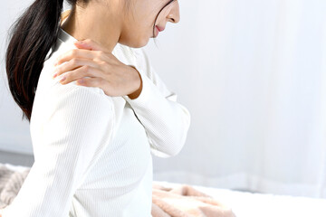 ベッドの上で肩こりに悩むアジア人女性 © koumaru