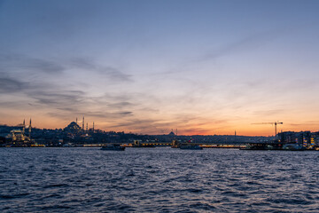 High resolution panoramic photograph capturing Istanbul's historic peninsula bathed in a crimson sunset glow. The city's iconic skyline silhouettes against the vibrant evening sky
