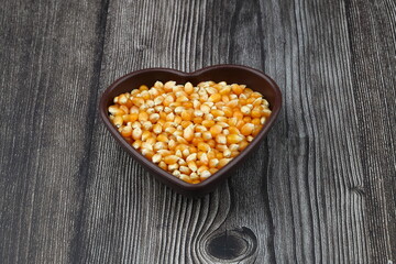 Unpopped popcorn in a wooden bowl on wooden background. A type of corn that expands from the kernel and puffs up when heated. Yellow seeds, edible, raw and vegan food. Isolated macro photo close up.