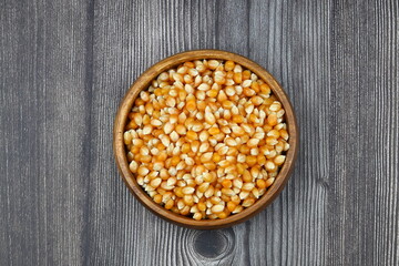 Unpopped popcorn in a wooden bowl on wooden background. A type of corn that expands from the kernel and puffs up when heated. Yellow seeds, edible, raw and vegan food. Isolated macro photo close up.