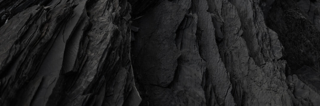 Black rock background. layered mountain surface close up. dark stone texture. cracked layers of slate