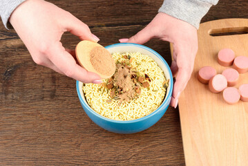 A young woman sprinkles a mixture of salt, pepper and other spices on instant noodles.