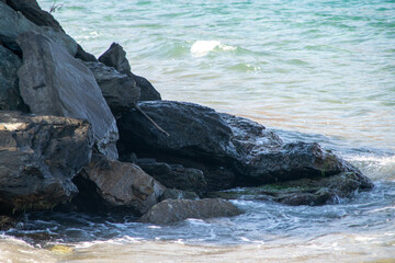 Envision a tranquil beach where rugged rocks meet the shore. The sun casts a golden glow, and the rhythmic waves create a soothing soundscape, inviting you to pause and appreciate the beauty of this r