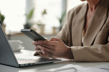 Hands of experienced female solopreneur texting in smartphone or looking through online information