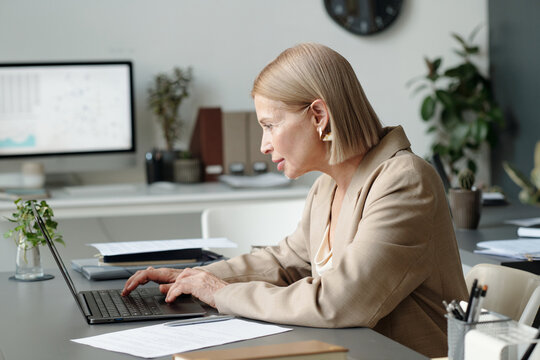Side view of mature businesswoman in formalwear looking at laptop screen while analyzing online data