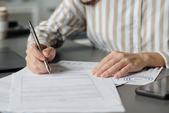 Hands of young unrecognizable female broker with pen reading terms of business contract before signing it