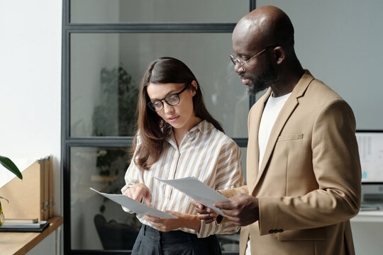 Two young intercultural analysts looking through paper documents with graphic data during discussion