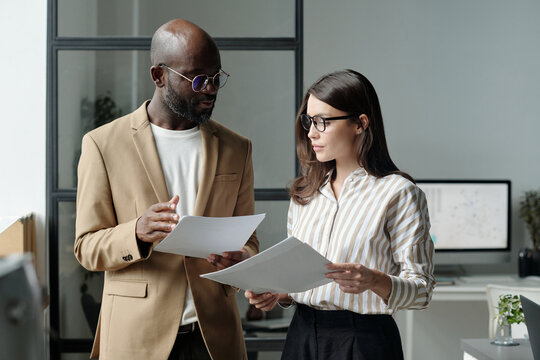 Confident young male broker or economist with financial papers discussing data with female colleague