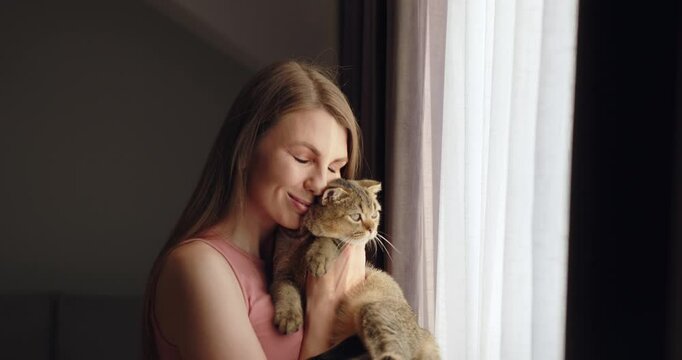 An Adorable Cuddly Cat Being Embraced by Its Loving Owner Within a Cozy and Welcoming Setting. This heartwarming video shows the bond between a woman and her cat, gentle pets in a serene setting