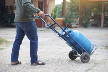 Close up man carries small cart that load blue gas cylinder tank  to make delivery to local...