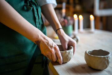 Hands of woman potter shaping clay bowl, deepening bottom on table. Craftswoman focused work in pottery workshop. Crafting with skill, traditional pottery school, hands at work, clay craftsmanship