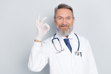 Senior male doctor showing approval gesture in medical uniform with grey background