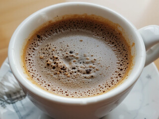 Obraz premium A close-up of a freshly brewed cup of coffee with a rich crema layer and tiny bubbles on the surface. The warm tones and creamy texture evoke a comforting coffee experience