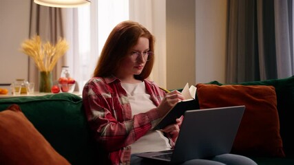 Busy concentrated Caucasian woman female girl at home student freelancer writing notes in notebook write schedule to do list noting information looking laptop using computer online e-learning at home