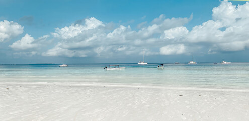 Fototapeta premium A beach with a few boats in the water. The sky is cloudy and the water is calm