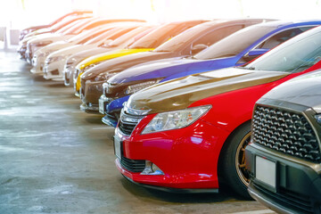 Obraz premium A diverse collection of cars stands proudly in a brightly lit parking area. Each vehicle shines under the sun, reflecting its unique color and design, attracting automotive enthusiasts