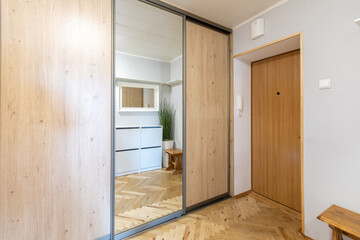 Modern Home Entrance Hallway With Wooden Furniture and Closet Mirrors. Home Interior. Bright and organized entryway with wooden recessed closet doors and decorative mirror in a minimalist design