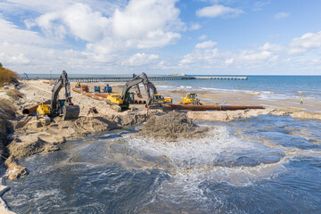 Beach restoration sand Bulldozers. Mud flows from the pipe with excavator behind for the...