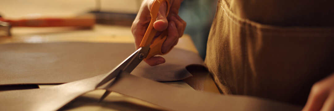 Close-up of person's hands cutting leather with scissors in workshop providing detailed view of leather crafting process