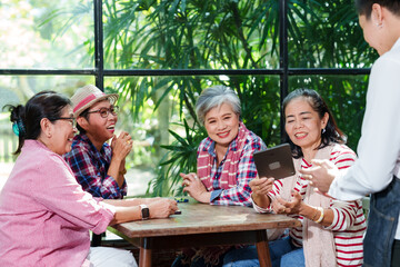 Senior Asian woman with close friend after retirement laughing while looking at tablet. Group of elderly women enjoying modern technology at cafe, sharing stories in joyful. Heartwarming moment.