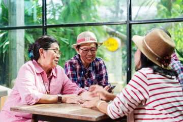 Senior Asian woman with close friend after retirement laughing at cafe. Elderly group enjoying lighthearted conversation, creating warm memories together. Genuine connection and happiness in a relaxed