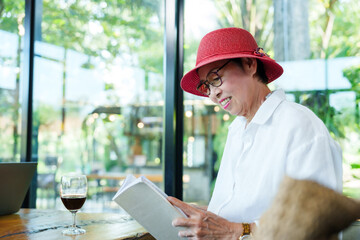 Elderly Asian woman relaxing after retirement reading a book at cafe. Senior enjoying quiet time...