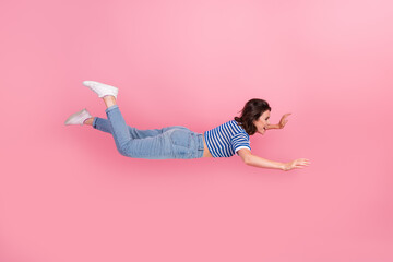 Young woman floating joyfully against a pink background, styled in casual denim and stripes, showcasing playful energy
